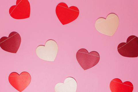 Red, white, and light pink paper hearts laying on a pink background.