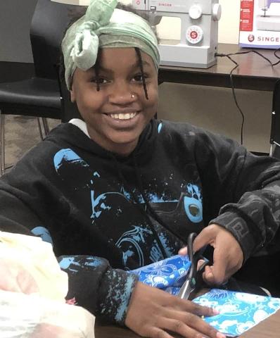 Smiling teenager cutting fabric for sewing class.