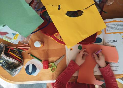 table with colored papers, pencil bag, scissors, and children's hands 