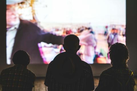 Silhouette of three people in front of movie screen. The movie is blurred out.