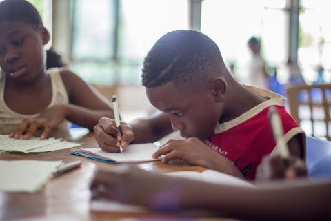 photo of tween boy writing in a notebook with a pencil.