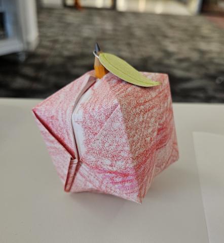 apple shape folded using origami method. Colored with crayons, with a pencil as the stem.