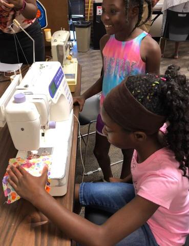 Teen girl sewing on a sewing machine at the Cherokee Library.