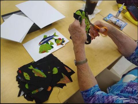 A Senior's hands making art from fabric scraps at a table.