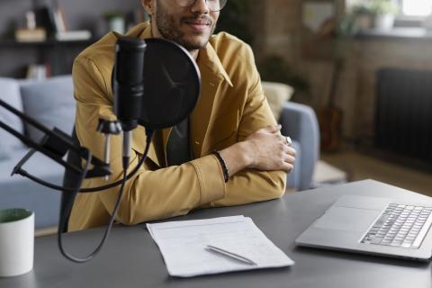 Young man sits at a desk in front of a microphone