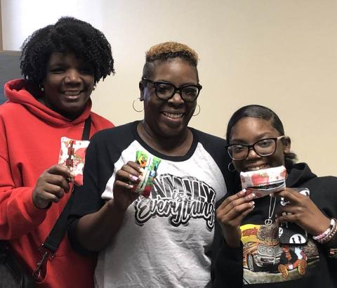 Three people proudly holding up their completed projects at the end of the Cherokee Sewing Club.