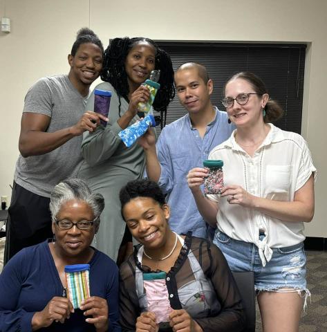 Six diverse, smiling people from the Cherokee Sewing Club pose with their completed project for the day.