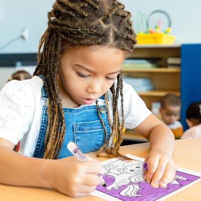 photograph of a young girl coloring in a coloring page with a purple marker