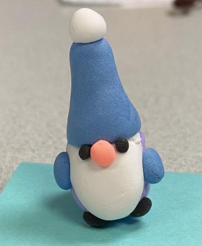 Tiny gnome made of air dry clay, with tall blue hat, white beard, black shoes. 