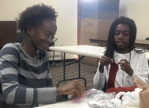 Woman in striped sweater and boy in white sweatshirt practice crochet stitches in the Cherokee library meeting room.