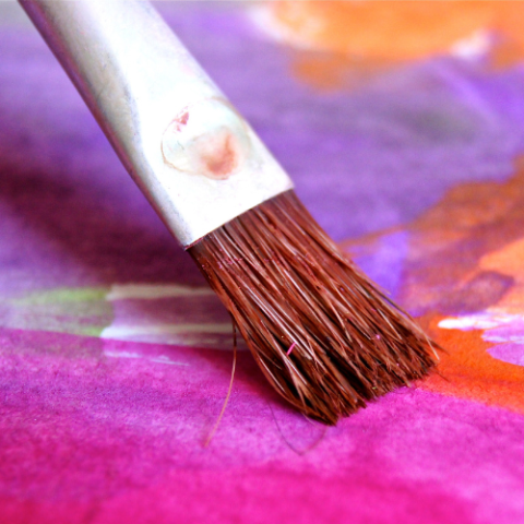 Close up of paint brush going over canvas of purple and pink paint.