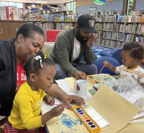 Two parents at the Cherokee Library help their toddlers with painting at a story time craft.