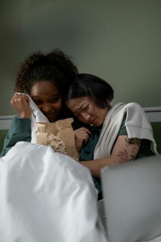 Two people sitting on a couch, eating popcorn simi hiding their facess 
