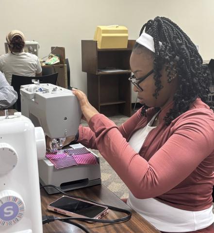 Woman in pink shirt adjusts her sewing machine prior to sewing at the Cherokee Library