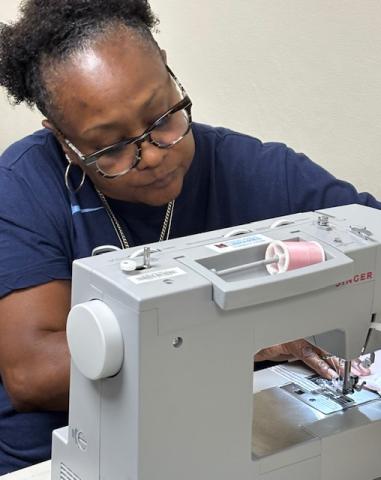 Woman in blue shirt concentrates intently as she works on a library sewing machine