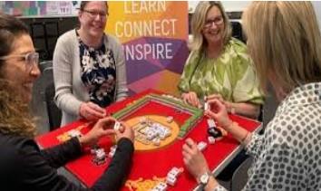 Four smiling ladies playing Mah Jong at table with bright red cloth.