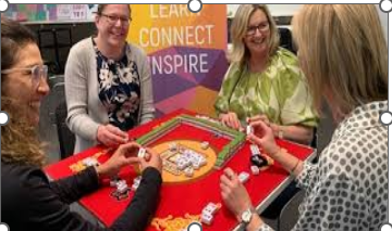 Four ladies playing Mah Jong at a red-topped table.