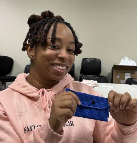 Woman in pink shirt holds a blue snap wallet she just finished at the Cherokee Library Sewing Club.