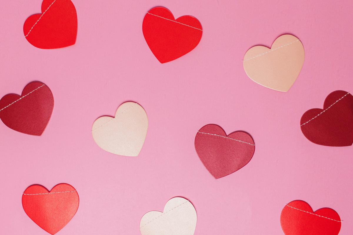 Red, white, and light pink paper hearts laying on a pink background.