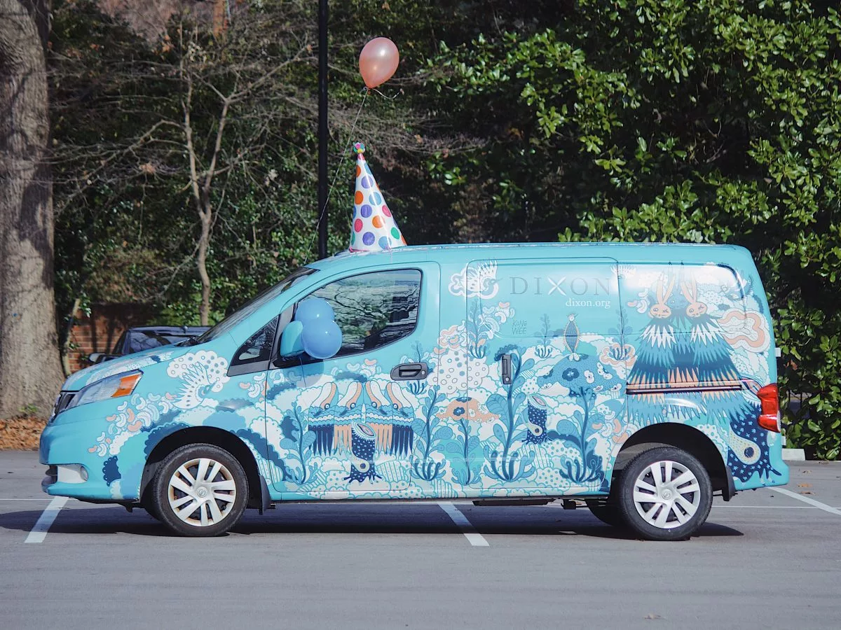 Dixon Art to Grow van with blue background, art decals covering the van, and a party hat on the hood of the van.