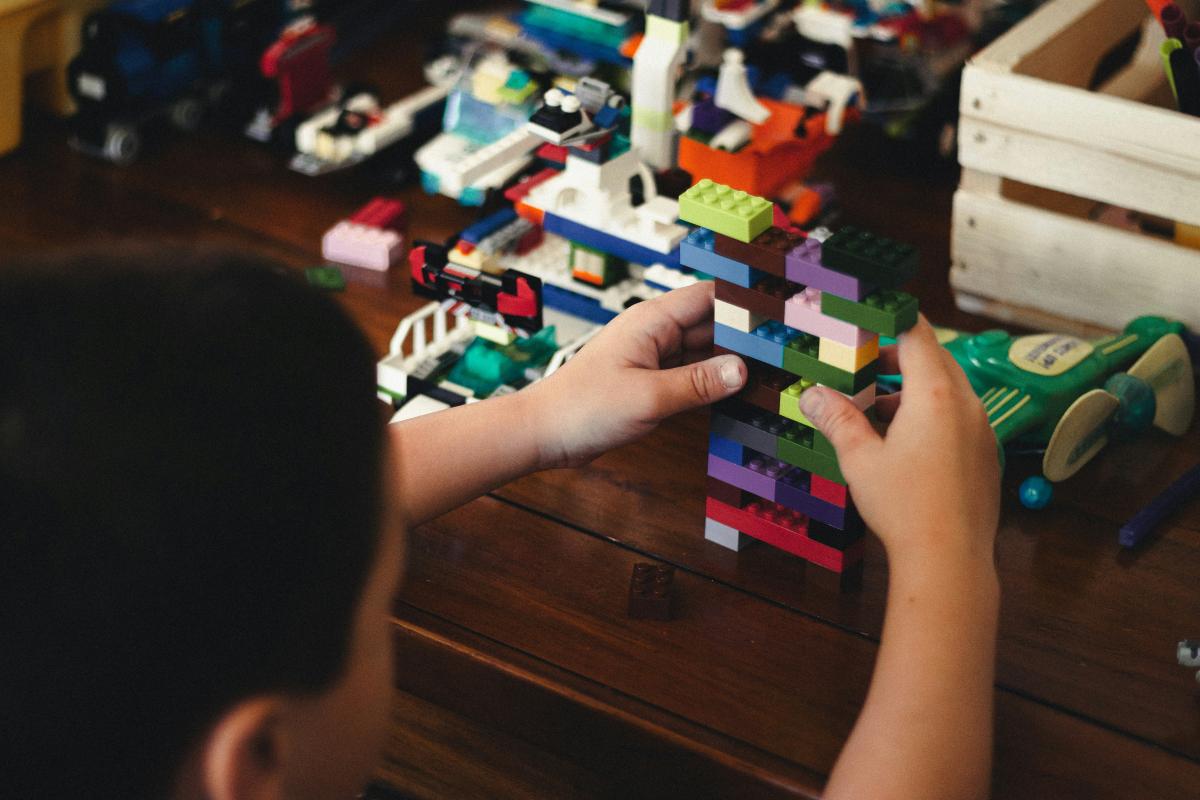 Child's hands holding lego pieces, with more scattered on table before him.