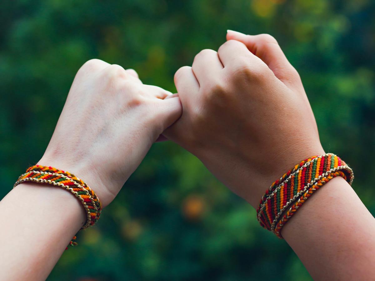 two hands, pinkies linked, with friendship bracelets on the wrists.