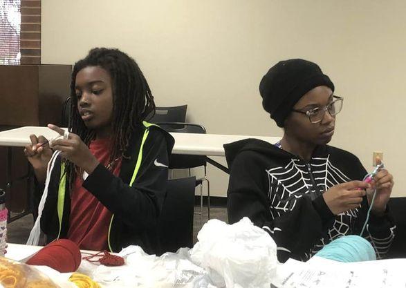 Two people sit at a table in the Cherokee Library, practicing crochet skills.