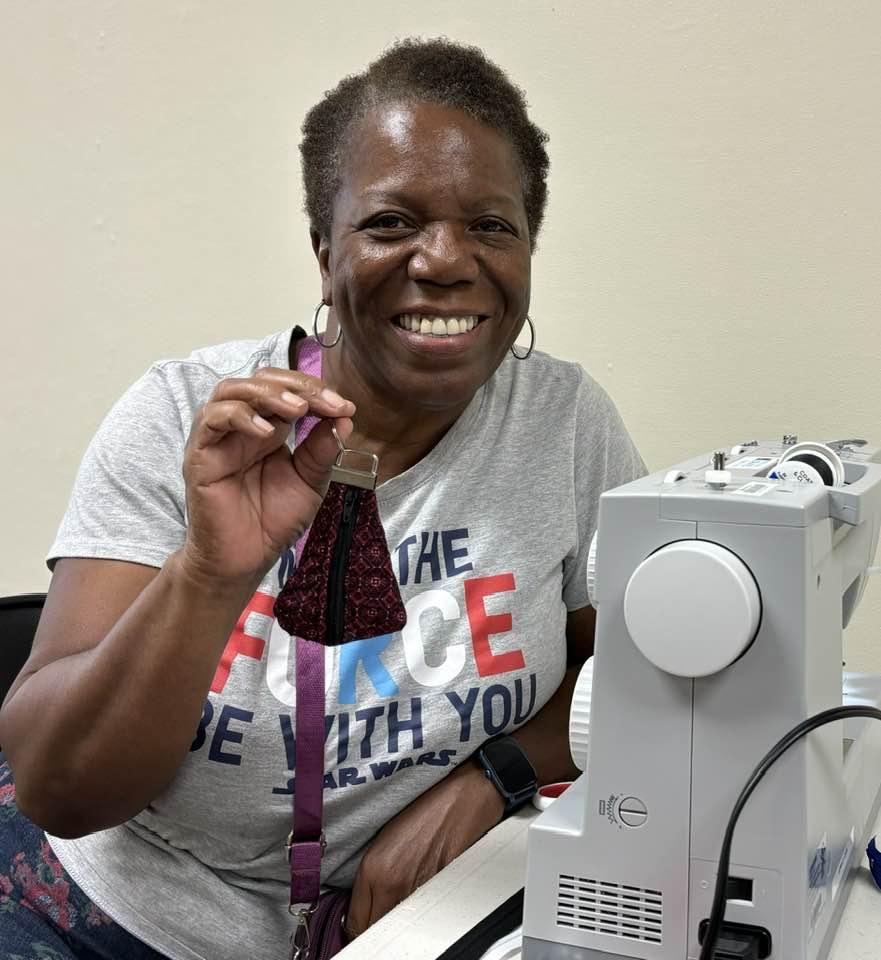 Happy woman in gray shirt holds up her finished sewing project.