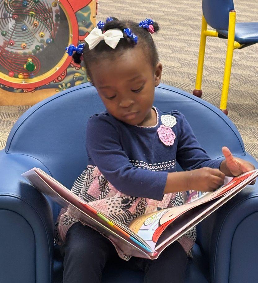 Toddler in blue dress looks at a book during story time at the Cherokee Library.