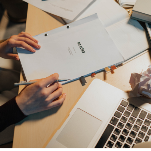Person with film script in hands. Laptop and crumpled paper next to them.