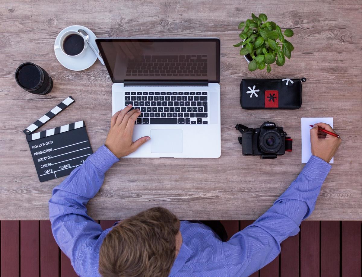 man sits at a desk with a laptop and filmmaking supplies