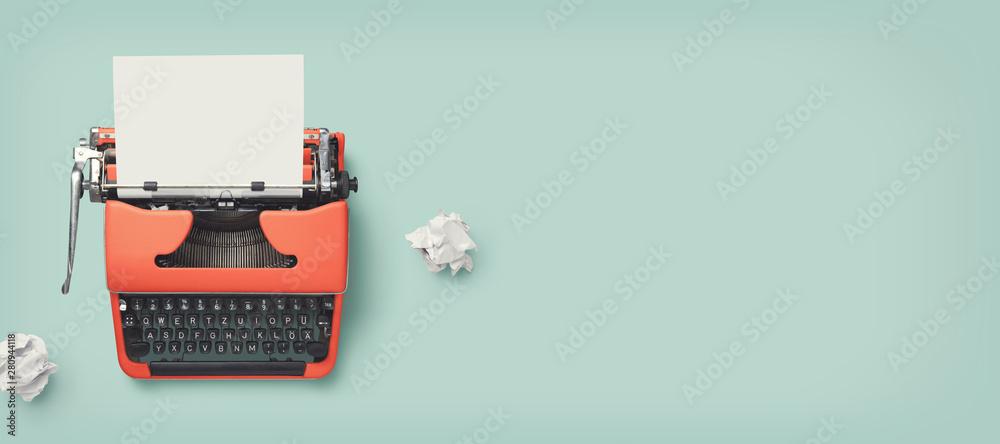 a type writer against a teal background with two pieces of crumpled paper nearby