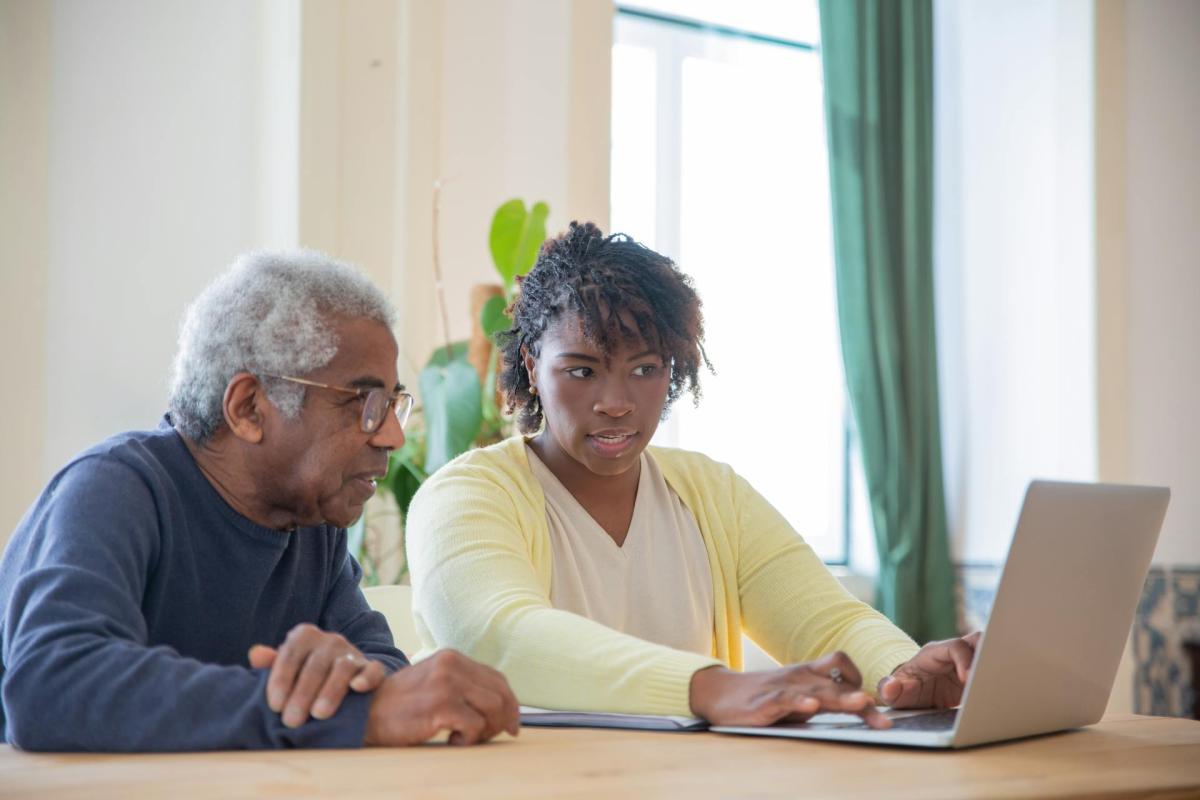 A senior and adult sit next to each other while using a computer.