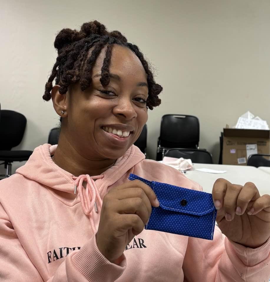 Woman in pink shirt holds a blue snap wallet she just finished at the Cherokee Library Sewing Club.